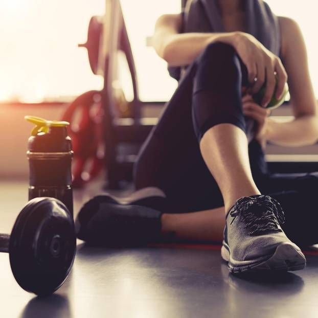 Persona sentada en el suelo de un gimnasio junto a una pesa y botella